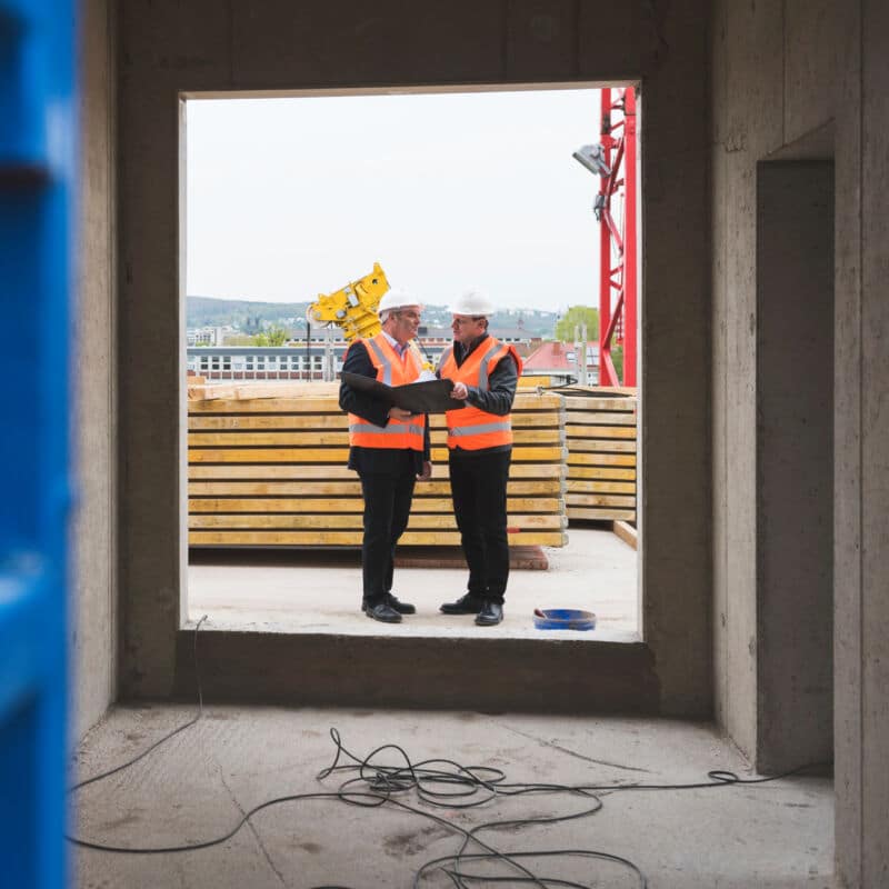 two-men-wearing-safety-vests-talking-in-building